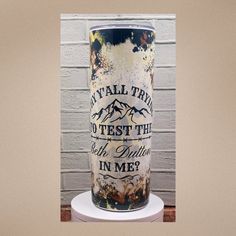 a tall vase sitting on top of a white table next to a brick wall with words painted on it