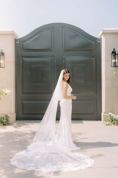 a woman in a wedding dress is standing by a large door with a veil on her head