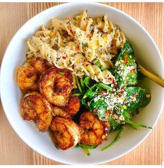 a white bowl filled with pasta, shrimp and spinach on top of a wooden table