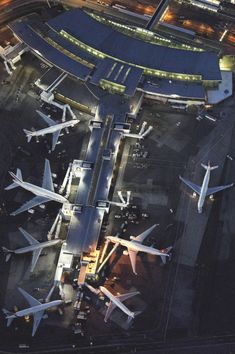 an aerial view of several airplanes parked at the airport terminal, with lights on in the background