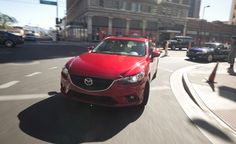 a red car driving down a street next to tall buildings