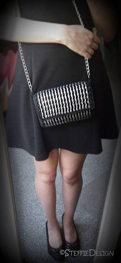 a woman in black and white dress holding a silver purse with chains on the bottom