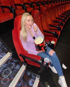 a woman sitting in a red chair eating popcorn and drinking soda while watching a movie