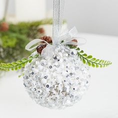 a christmas ornament hanging from a tree branch with pine cones and silver sequins