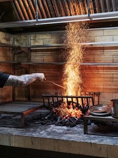 a man is cooking food over an open fire pit with tongs in his hand