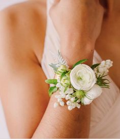 a close up of a person wearing a white flower wrist corsage with green and white flowers