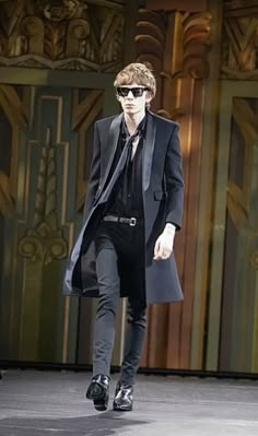 a man walking down a runway wearing sunglasses