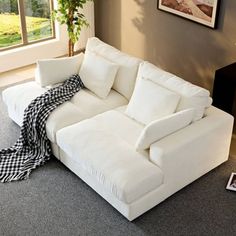 a white couch sitting on top of a carpeted floor next to a window with a black and white checkered blanket