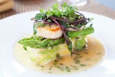 a white plate topped with scallops and broccoli covered in sauce on top of a table