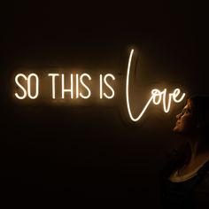 a woman standing in front of a neon sign that says so this is love