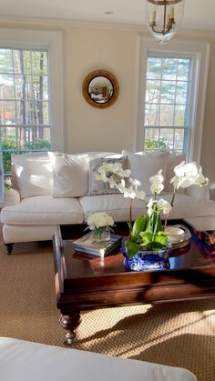 a living room filled with furniture and flowers on top of a coffee table in front of two windows