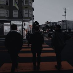 three people walking across a crosswalk in the evening