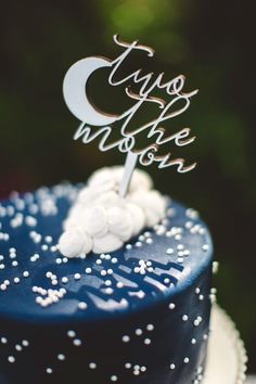 a blue cake topped with white frosting and a silver topper that reads, i love you to the moon