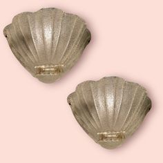 two scallop shells are shown against a light pink background, one is gold and the other is silver