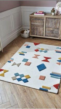 a white rug with colorful blocks on it in the middle of a wooden floor next to a dresser