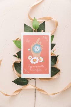 there is a card with a clock on it next to some leaves and ribbon around it