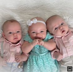 three baby dolls laying on top of a white blanket