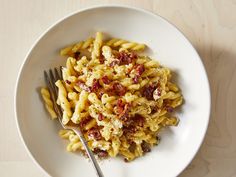 a white plate topped with pasta covered in cheese and bacon next to a fork on top of a wooden table