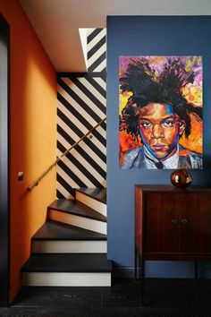 a painting is hanging on the wall next to a wooden dresser and stairs with black and white striped walls