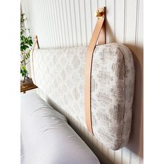 a white bed with a brown leather strap hanging on the wall next to two pillows