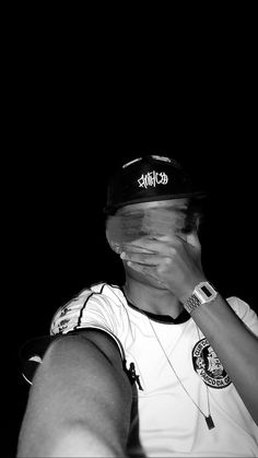 black and white photograph of a person covering their face with his hands while wearing a baseball cap