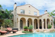 a house with a swimming pool and lounge chairs in the front yard, surrounded by palm trees