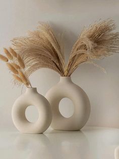 two white vases sitting on top of a table filled with dried grass and plants