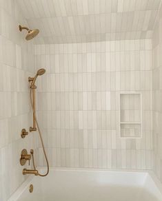 a white tiled shower with gold faucet and hand held shower head in the corner