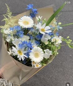 a bouquet of blue and white flowers is held by someone's hand on the street