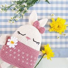 a crocheted stuffed animal sitting next to flowers on a blue and white checkered tablecloth