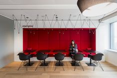 a woman sitting at a table in an office setting with red walls and black chairs