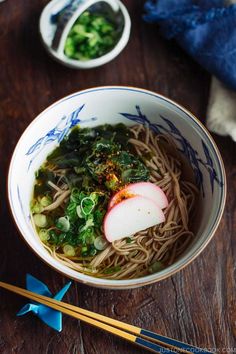 a bowl filled with noodles and vegetables next to chopsticks on a wooden table