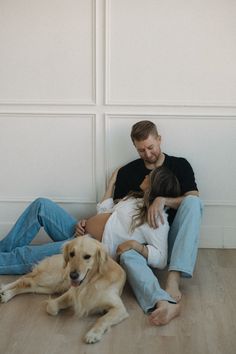 a man and woman cuddle on the floor with their dog, who is laying next to them