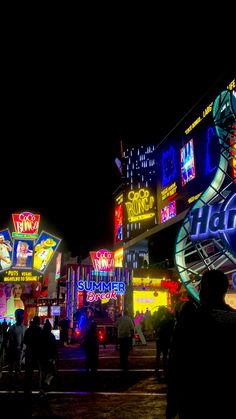 many people are walking around in front of some buildings at night with brightly lit signs on them