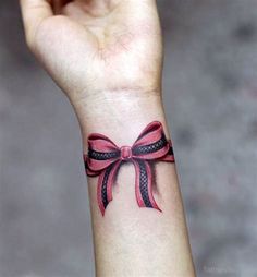 a woman's wrist tattoo with a pink ribbon on it and a black bow