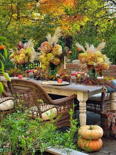 an outdoor dining area with wicker furniture and pumpkins on the table, surrounded by greenery