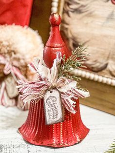 a red bell with a tag on it sitting on a table next to a christmas tree