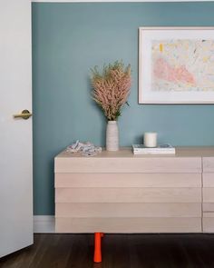 a white dresser sitting in a room next to a painting on the wall and a vase with flowers