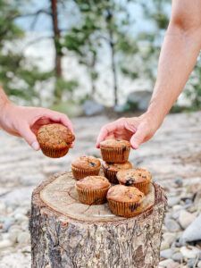 two hands reaching for muffins on top of a tree stump