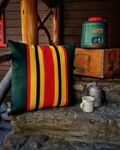 a striped pillow sitting on top of a wooden bench next to a cup and mug