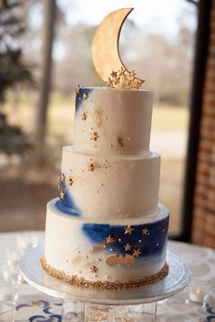 a three tiered cake with gold stars and a crescent decoration on the top layer