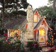 a small house with christmas lights on the windows and door is surrounded by greenery