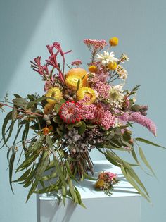 a vase filled with lots of colorful flowers on top of a white table next to a blue wall