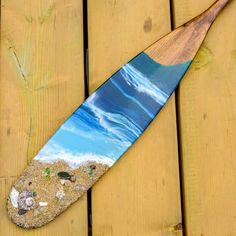 a wooden paddle sitting on top of a beach covered in sand and sea shells next to the ocean