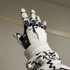 a gloved hand with an electronic device attached to it's palm, in front of a white wall