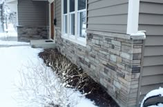 a house with snow on the ground next to it and bushes in front of the house