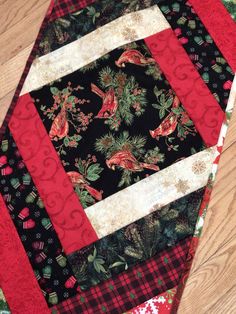 a quilted table runner with red and black fabrics on it, sitting on a wooden floor