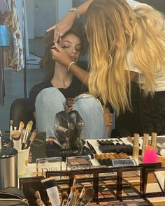 two women sitting in front of a table with makeup and cosmetics on top of it