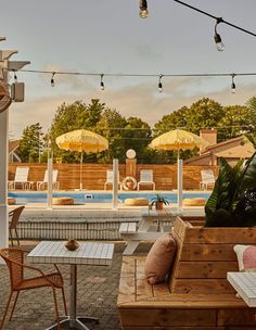 an outdoor seating area with tables and umbrellas over looking the swimming pool at sunset