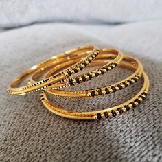 "* Handcrafted Gold Plated 4 Bangle Set. Sold as a set. * Bangles with pretty black beads and gold beads * High Quality 22 K Gold Plated- 4 Bangle set * Bangles Sizes : 2.4 inches= ( 2.25\" diameter of the inner circle) ; 2.6 inches = ( 2.45\" diameter of the inner circle); 2.8inches = (2.54\" diameter of the inner circle) Gorgeous gold-plated bangle/ bracelet best exemplifies the careful craftsmanship done on it -- a specialty at Nemali Jewelry. It has a special tone of elegance attached to it. Black Gold Bangles, Black Beads Bangles Gold, Black Beads Bangles Gold Indian, Black Beads Bangles, Beads Bangles, Wedding Bangles, Black Bangle, Kundan Bangles, Bridal Jewellery Design